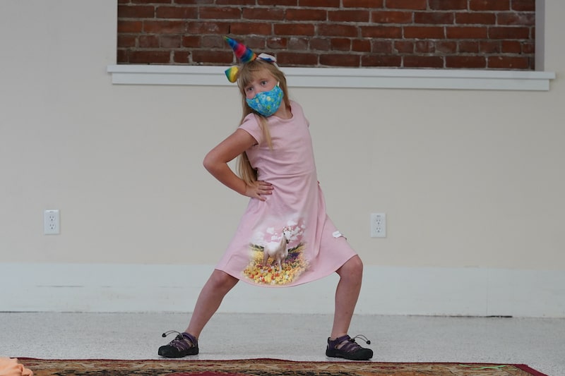 Girl in pink unicorn mask and matching dress stretching her legs out
